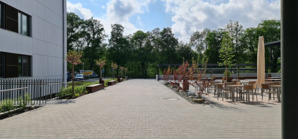 Haupteingang und Aufenthaltsbereich mit Pflanzbeet und Sitzbänken, Blick kommend aus der Schule