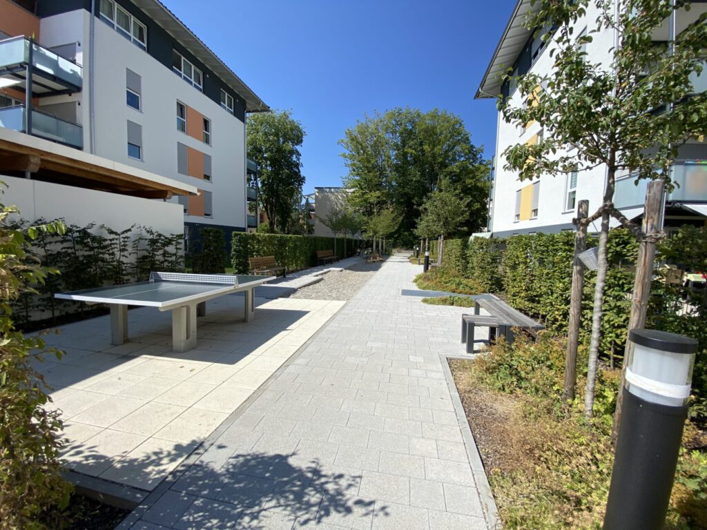 gepflasterte Wegefläche im Wohnquartier mit Bänken und einer Tischtennisplatte, dient als mögliche Aufenthaltsfläche