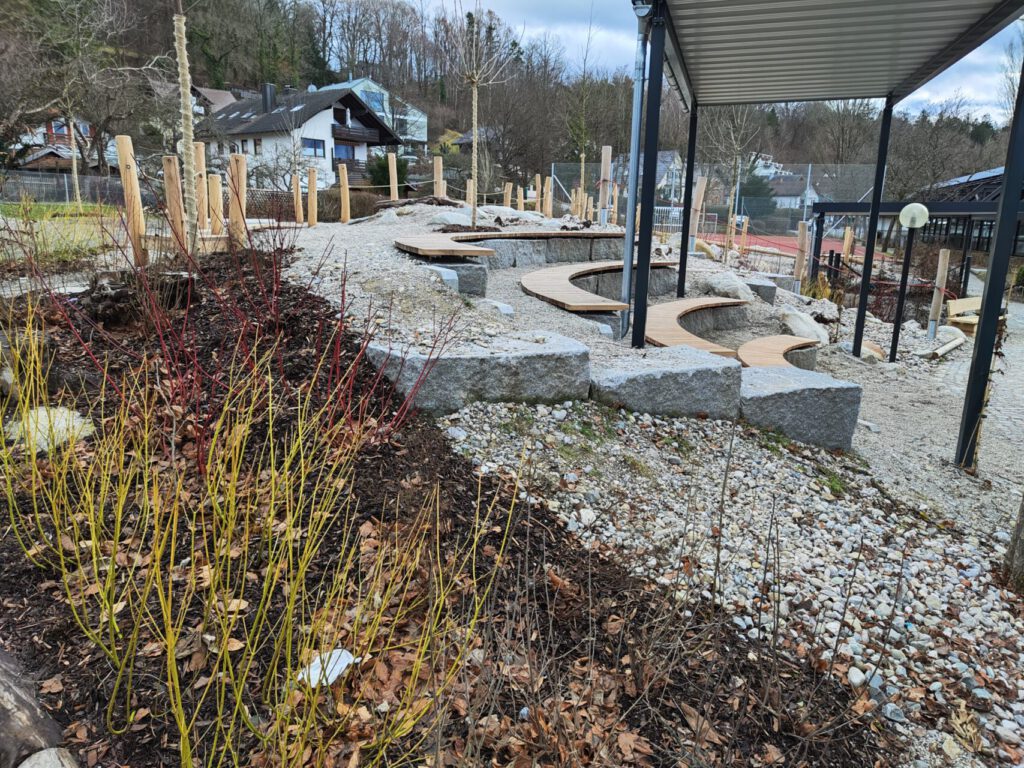 Sitzatrium aus Natursteinblöcken mit Holzauflagen und Überdachung
