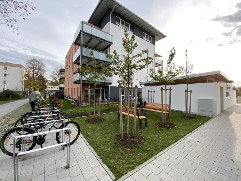 kleine Rasenfläche mit Bänken und Baumpflanzungen als Treffpunkt, mit Fahrradstellplätzen